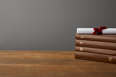 Brown books and diploma with red ribbon on wooden surface on grey