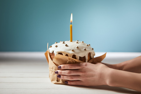 cropped view of woman holding easter cake decorated with sprinkles and burning candle on turquoise