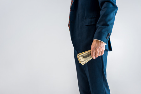cropped view of mature businessman standing in formal wear and holding dollar banknotes isolated on...
