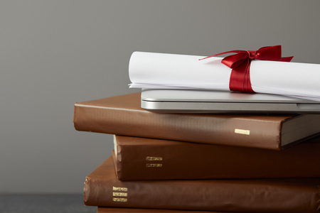 Brown books, laptop and diploma with red ribbon isolated on greyの写真素材