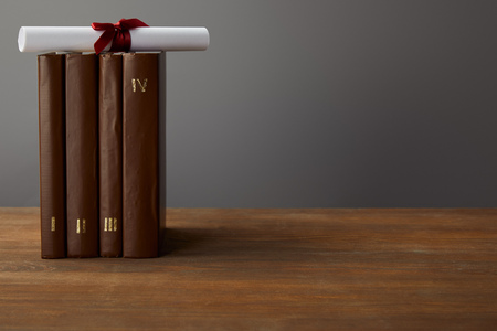 Brown books and diploma with red ribbon on wooden surface on grey