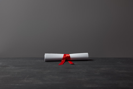 Diploma with red ribbon on dark textured surface on greyの写真素材