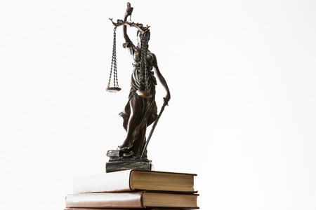bronze figurine with scales of justice on pile of brown books isolated on white