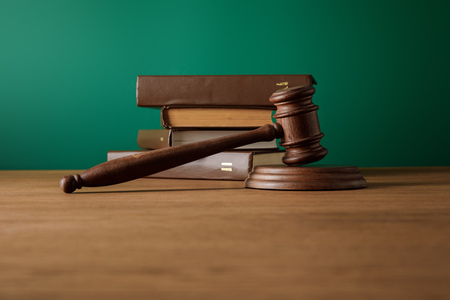 bottom view of volumes of brown books in leather covers and gavel on wooden table on dark green...