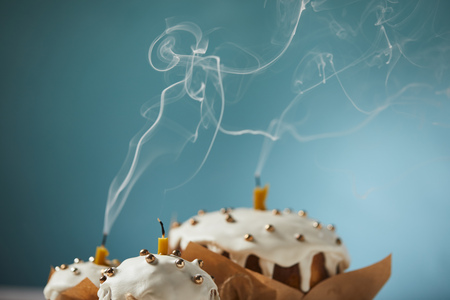 selective focus of decorated easter cakes with candles and smoke on turquoiseの写真素材