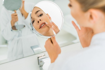 selective focus of woman touching face and looking at mirror in bathroomの写真素材