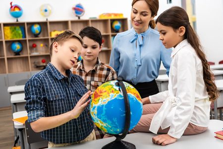 Teacher and pupils touching globe with smile while studying geography in classroomの写真素材