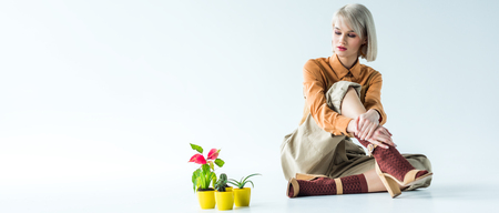 panoramic shot of beautiful stylish girl sitting with flower pots on white with copy spaceの写真素材