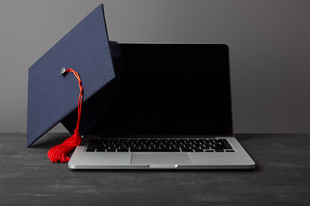 Laptop with blank screen and academic cap with red tassel on greyの写真素材