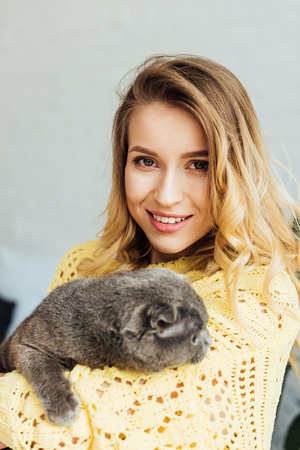 beautiful smiling girl in knitted sweater looking at camera and hugging adorable scottish fold catの写真素材
