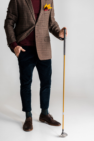cropped view of stylish mature man holding golf club and while standing with hand in pocket on greyの写真素材