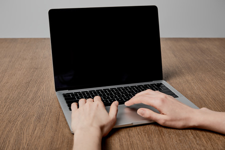 cropped view of woman using laptop with blank screen on wooden surface
