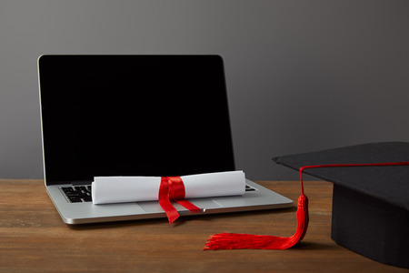 Laptop with blank screen, diploma and academic cap with red tassel on greyの写真素材