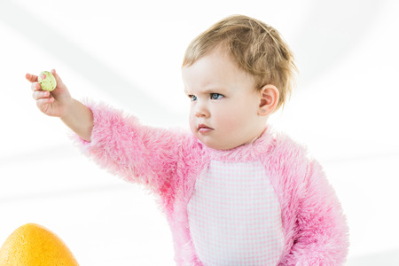 adorable baby holding colorful quail egg in outstretched hand isolated on whiteの写真素材