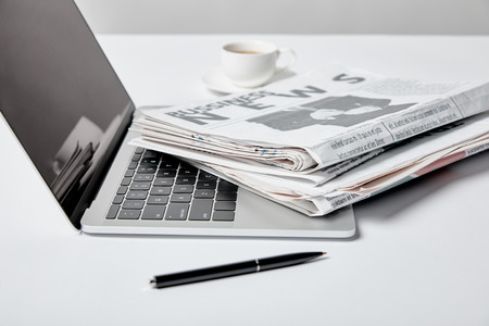 selective focus of laptop with blank screen near business newspapers, pen and cupの写真素材