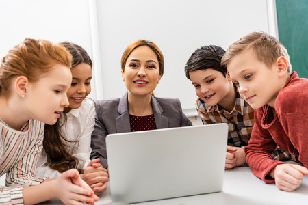 Smiling teacher and pupils using laptop during lesson in classroomの写真素材