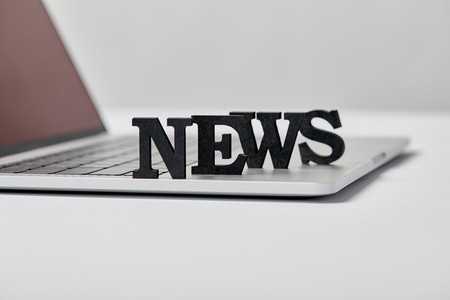 selective focus of black news lettering near laptop on grey