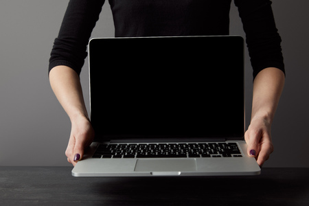 Partial view of woman holding laptop with blank screen on greyの写真素材