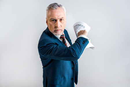 angry mature businessman holding business newspaper isolated on greyの写真素材