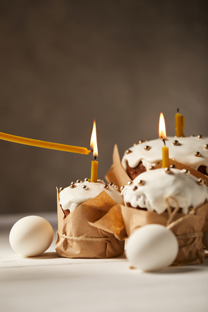 delicious easter cakes with burning candles and chicken eggs on white table