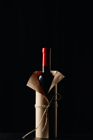 Wine bottle in paper wrapper on dark surface isolated on blackの写真素材