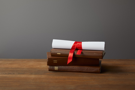 Brown books and diploma with red ribbon on wooden surface on greyの写真素材