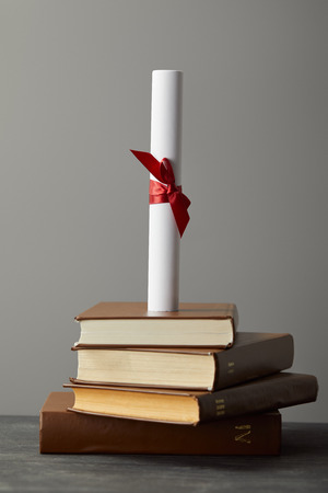 Diploma with red ribbon and books on textured surface isolated on greyの写真素材