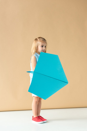 adorable kid playing with blue paper plane on beige backgroundの写真素材