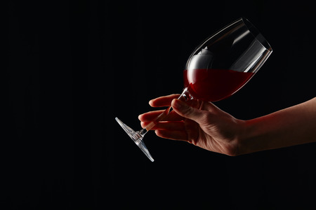 Partial view of woman holding wine glass with red wine isolated on blackの写真素材