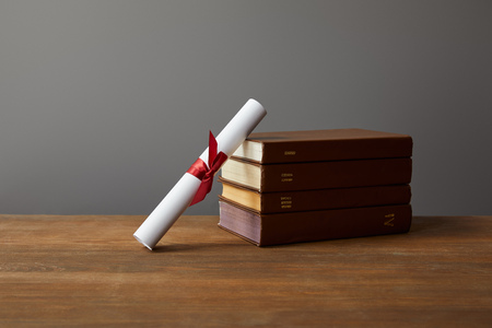Brown books and diploma with red ribbon on wooden surface on greyの写真素材