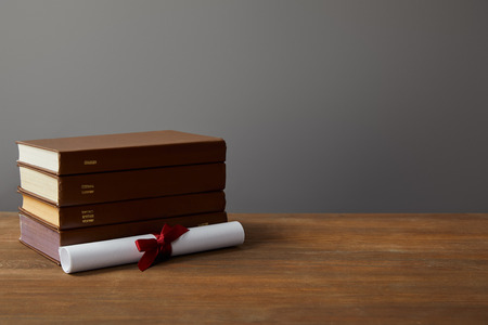 Brown books and diploma with red ribbon on wooden surface on greyの写真素材
