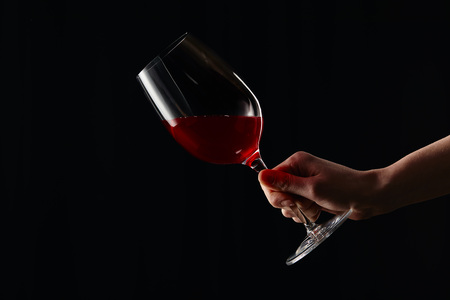 Partial view of girl holding wine glass with red wine isolated on black