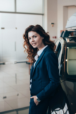 smiling businesswoman standing near car and looking at cameraの写真素材