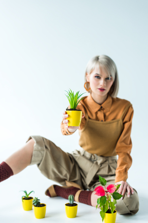 beautiful stylish girl holding flower pot and looking at camera on whiteの写真素材