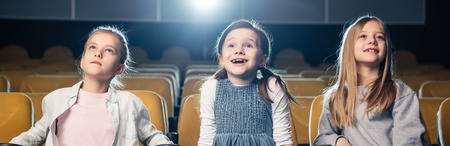 panoramic shot of smiling friends watching movie in cinema togetherの写真素材