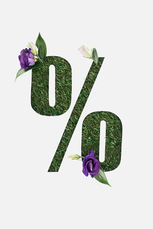 top view of cut out percent sign on green grass background with green leaves and purple flowers...