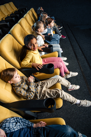 smiling multiethnic friends watching movie in cinema togetherの写真素材