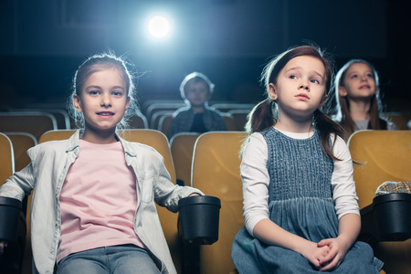 cute children sitting in cinema together with friends and watching movieの写真素材