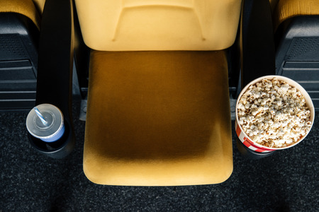 top view of orange cinema seat with paper cups of soda and popcorn in cup holdersの写真素材