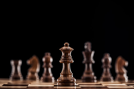 selective focus of brown wooden queen on chessboard isolated on blackの写真素材