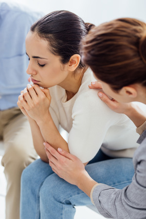 woman embracing depressed woman during therapy meetingの写真素材
