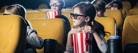 panoramic shot of children watching movie and holding paper cups with popcornの写真素材