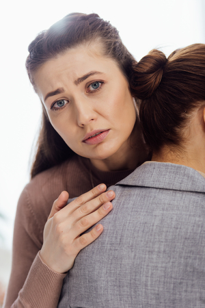 sad woman looking at camera while embracing another woman during therapy meetingの写真素材