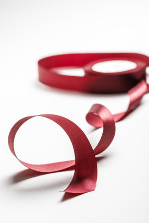 selective focus of silk wavy burgundy ribbon with spool on grey backgroundの写真素材