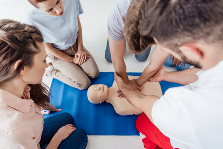 high angle view of instructor performing cpr on dummy during first aid training with group of people