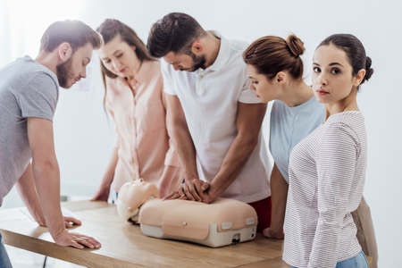 woman looking at camera while group of people performing cpr on dummy during first aid trainingの写真素材