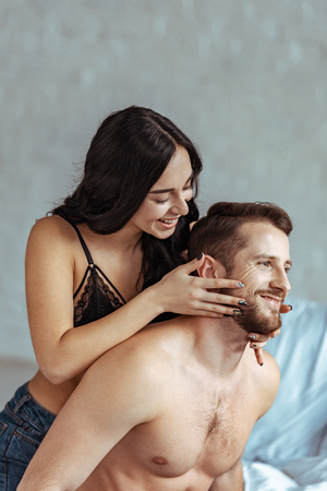 attractive woman and handsome shirtless man hugging and smiling in bedroomの写真素材