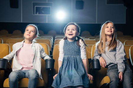 three adorable smiling kids watching movie in cinema togetherの写真素材