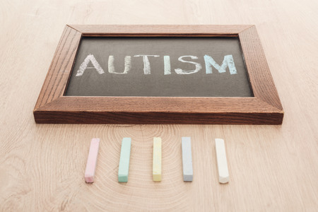 autism lettering written on chalkboard near multicolored chalks on wooden surface