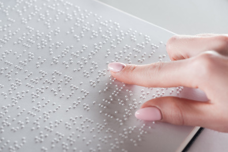 partial view of young woman reading braille text on white paperの写真素材